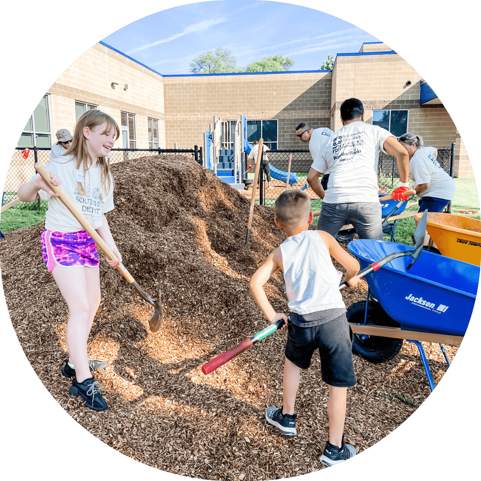 A group including kids working on moving mulch to cover playground floor