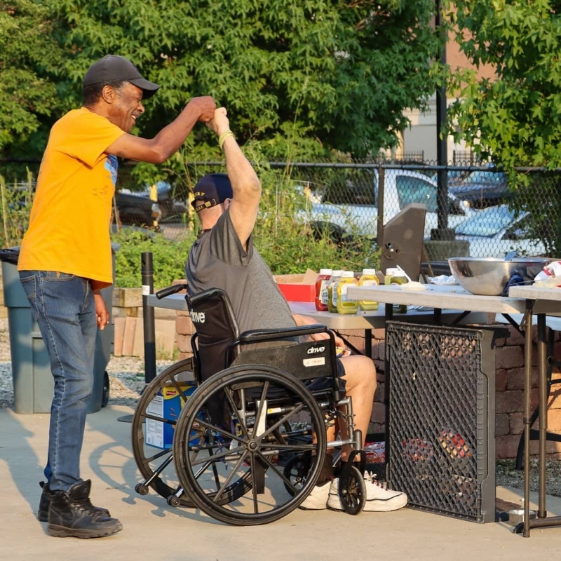 Two friends at a grill party and one of them is in wheelchair