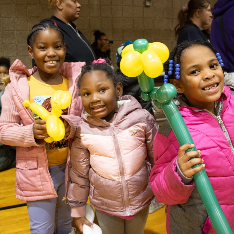 Three girls smiling holding balloons